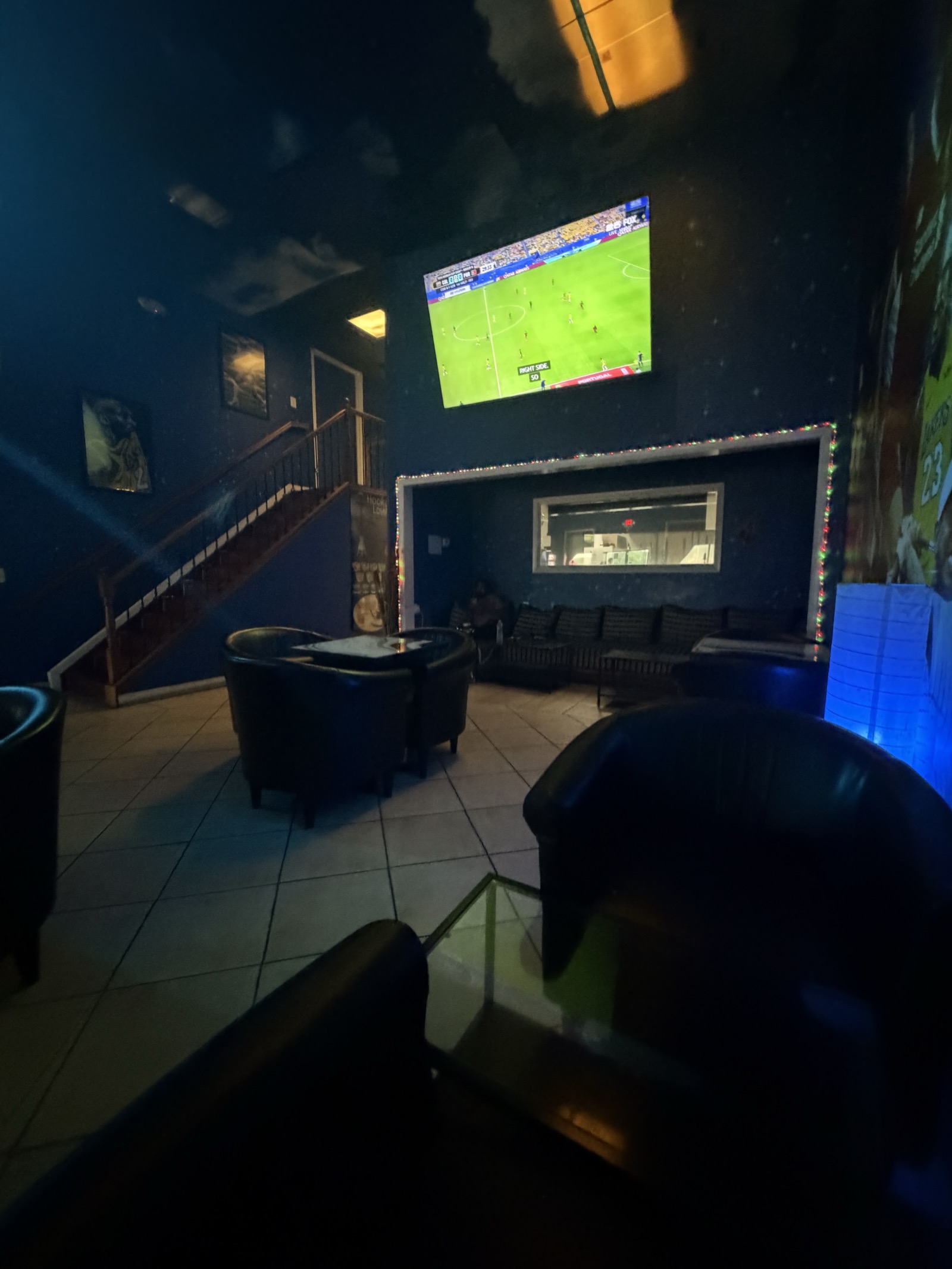 Soccer viewing corner with big screen TV, leather couches, and string lights